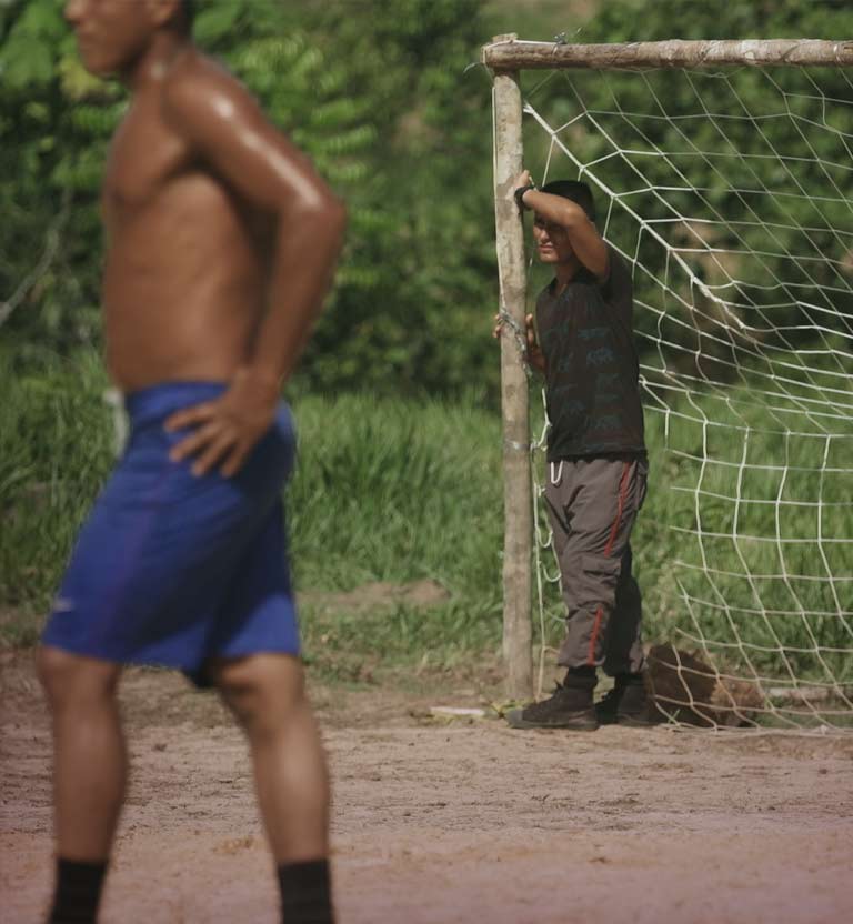 Hombre apoyándose en el arco de una cancha de fútbol en una zona rural.