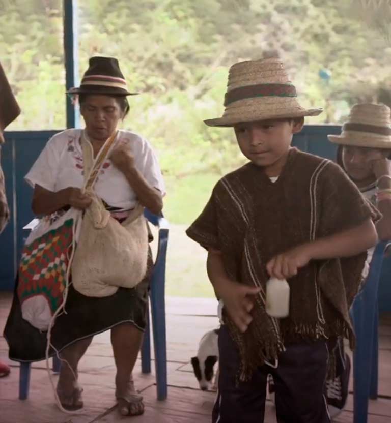 Niño indígena sosteniendo una botella y atrás una mujer indígena 