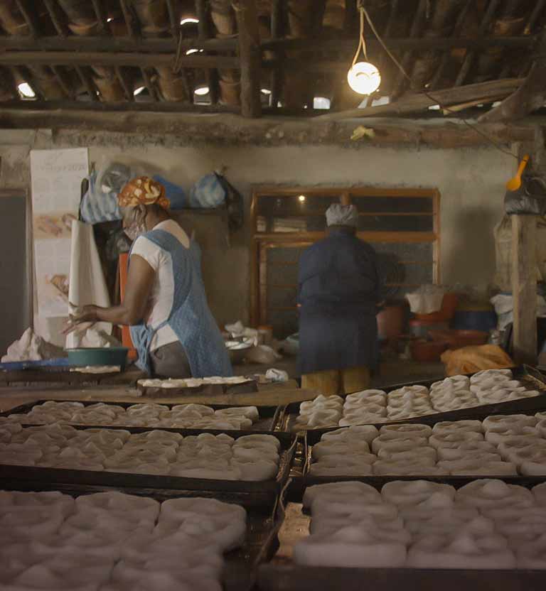 Dos  mujeres afrocolombianas cocinando con maíz en una casa rudimentaria 