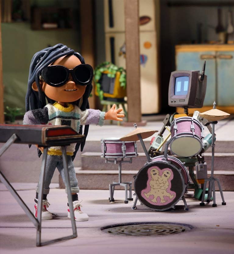 Personaje de niña tocando un teclado. Atrás un robot tocando la batería 