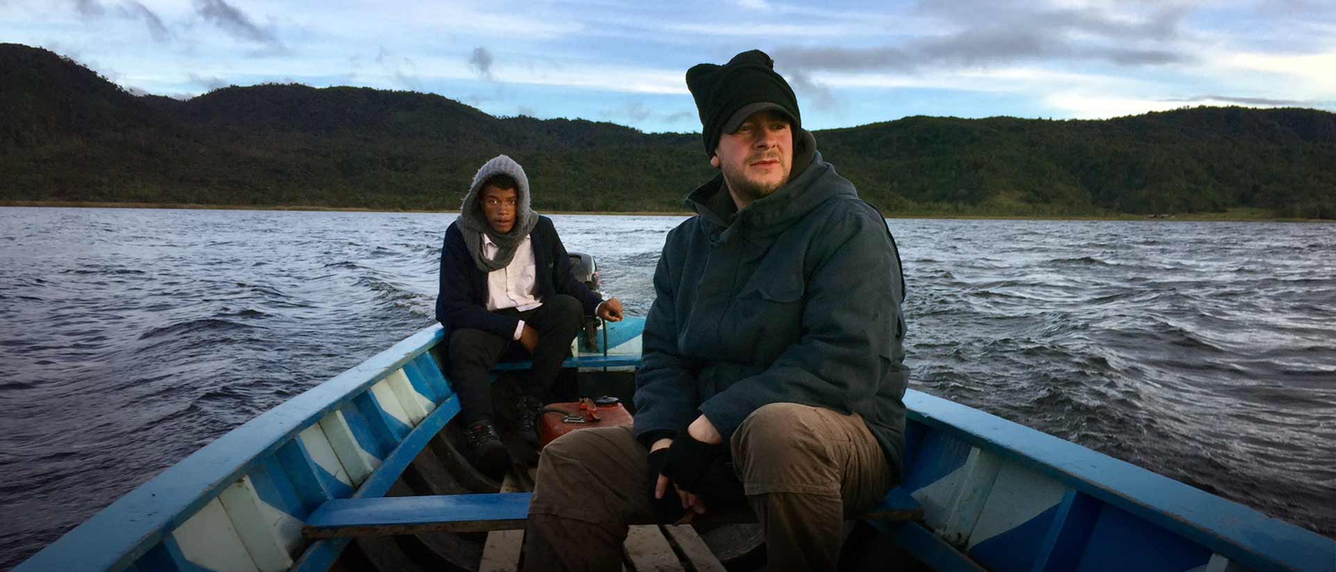 hombre afrodescendiente adulto junto a un hombre blanco adulto atravesando el río sobre una lancha
