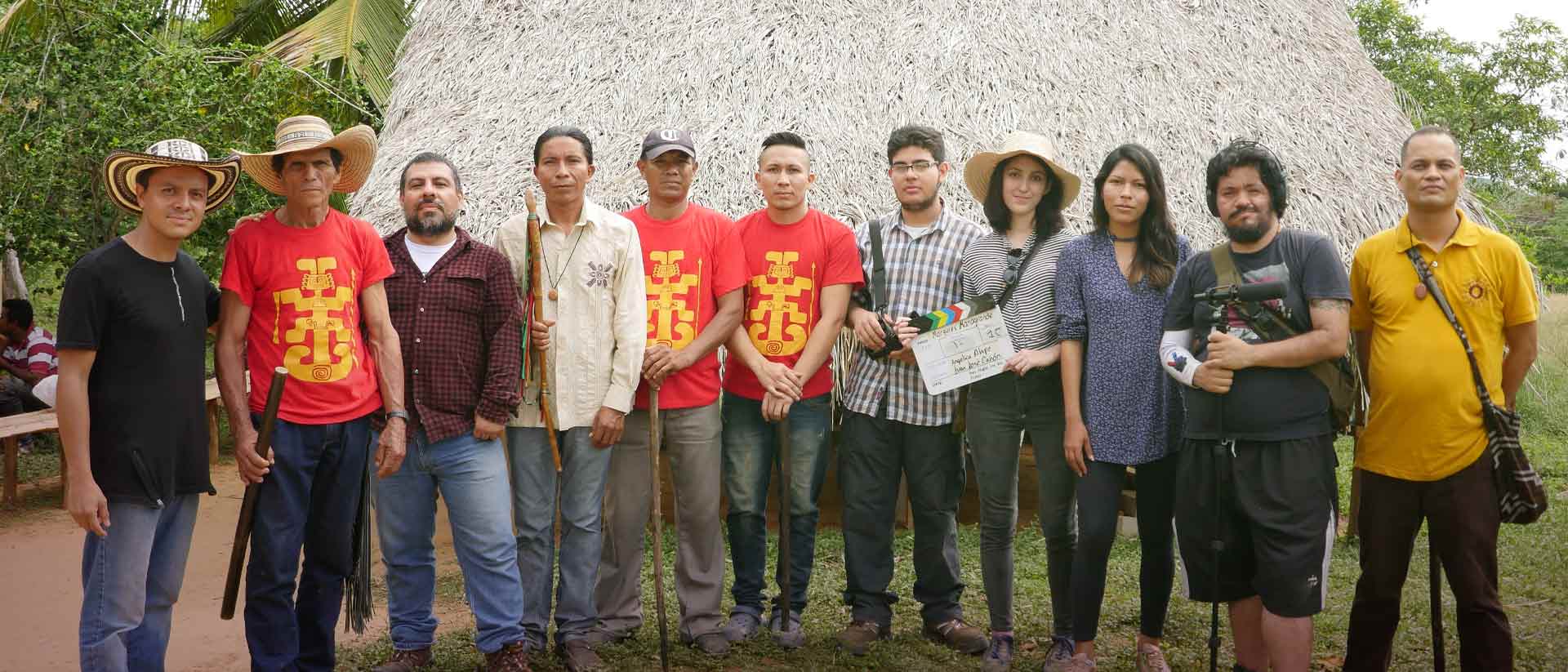grupo de personas, indígenas y equipo audiovisual, detrás de ellos una maloka