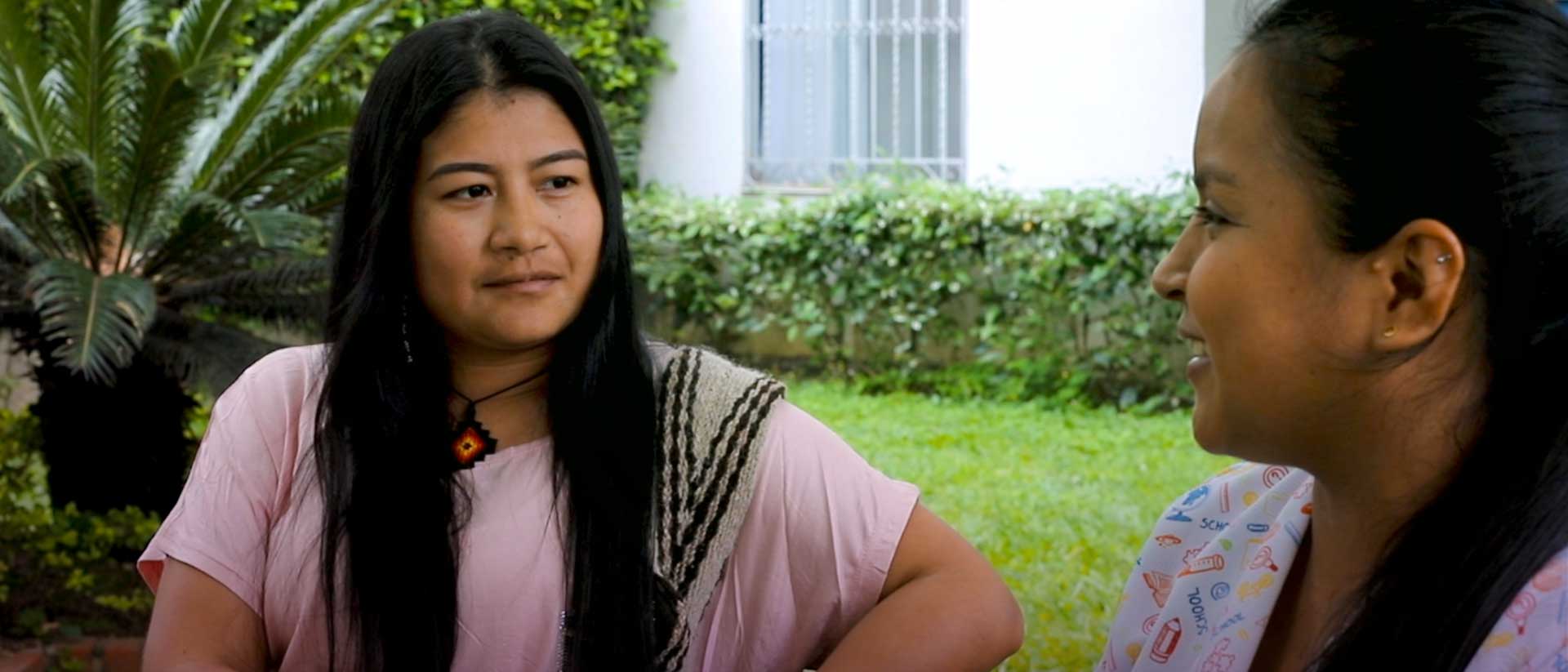 dos mujeres indígenas jóvenes sonriendo y hablando en un jardín