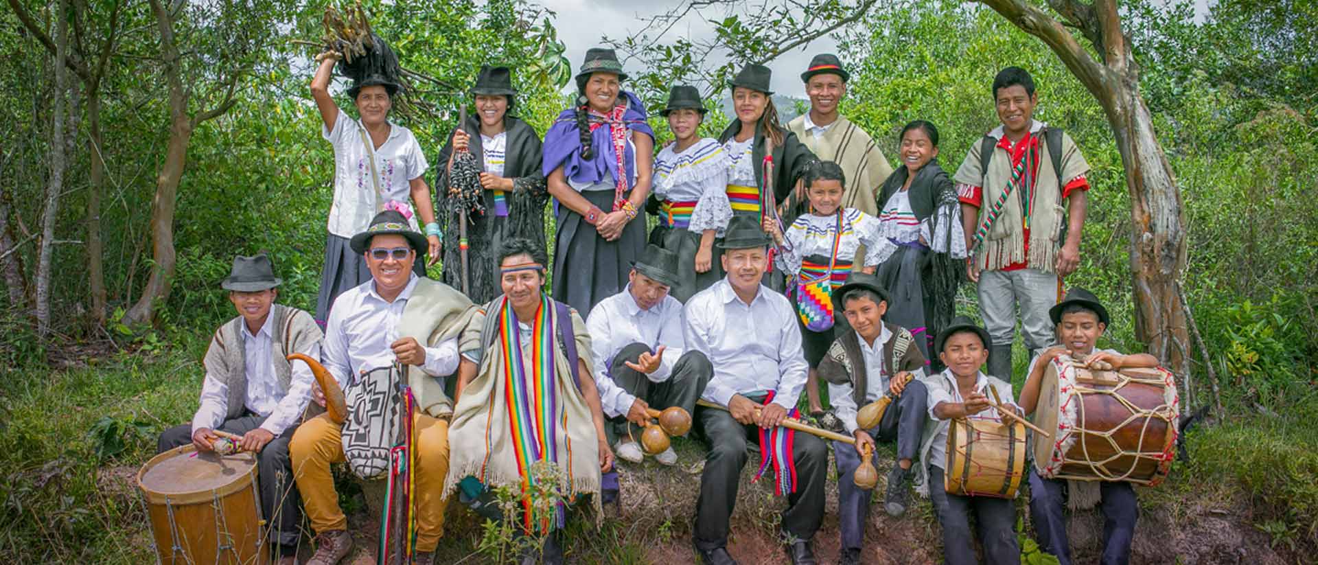 Indígenas sonriendo con trajes típicos e instrumentos 