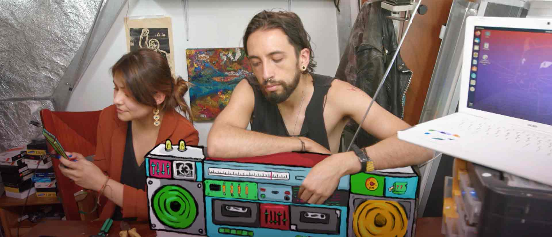 Joven sosteniendo una grabadora de doble cassette en sus piernas. A su lado una joven con un celular en la mano