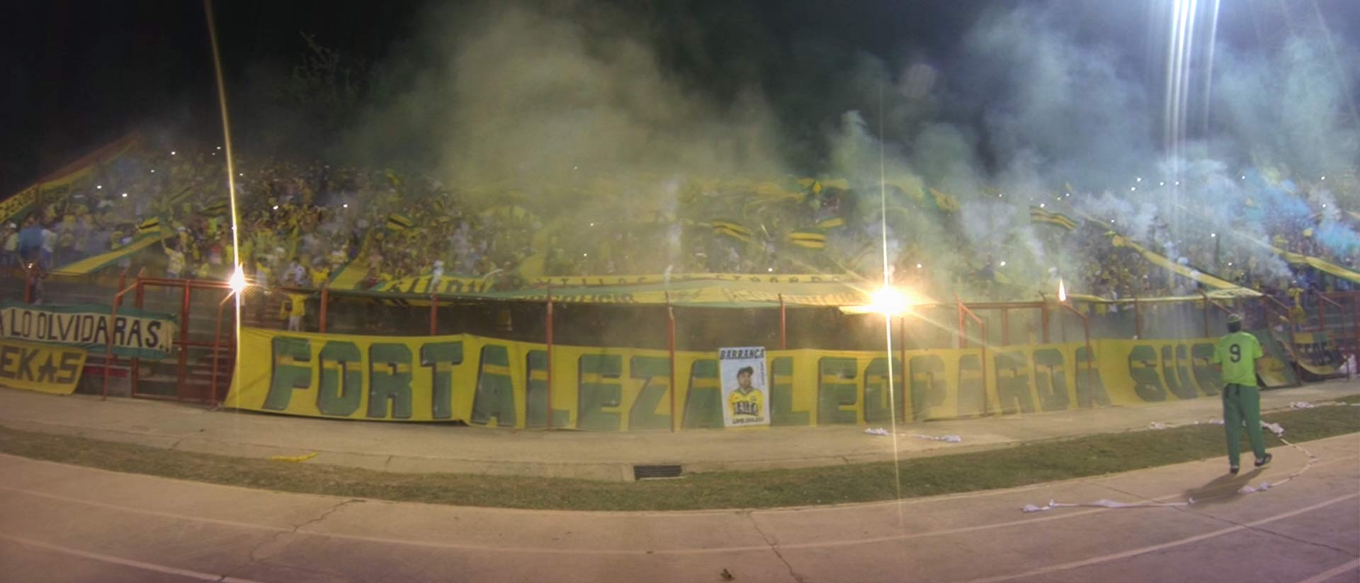 Hinchas de fútbol de la barra brava apoyando a su equipo con bengalas y trapos.