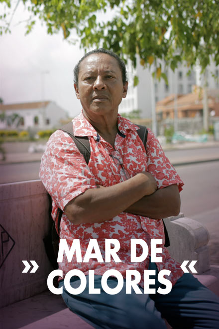 Hombre sentado en una banca en la calle, cruzado de brazos.