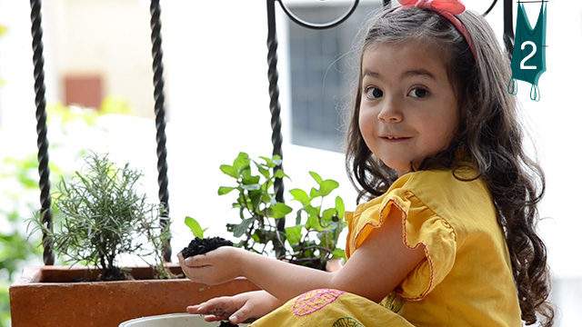 Niña sonriendo mientras siembra flores en el balcón
