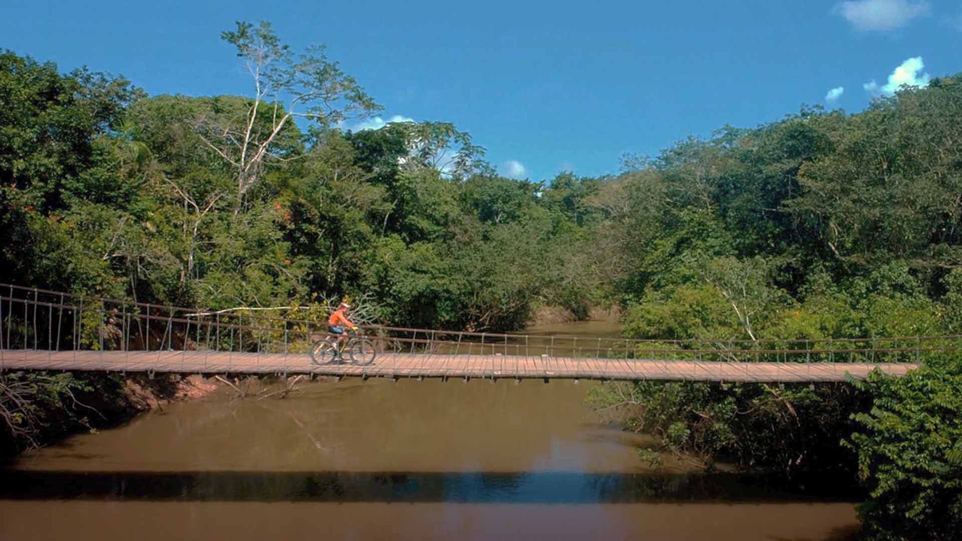 Ciclista cruzando un puente colgante sobre el río - Aislados