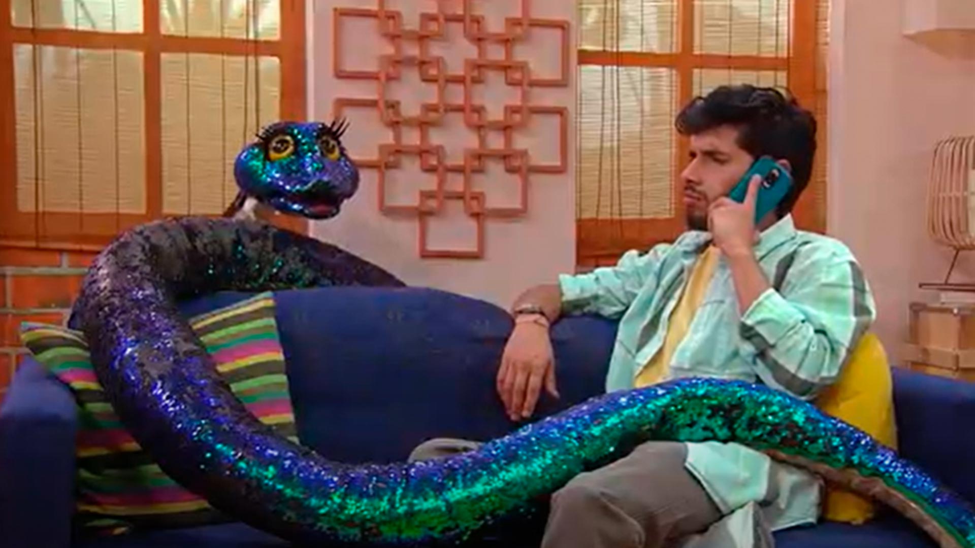 Hombre hablando por celular al lado de una serpiente de peluche 