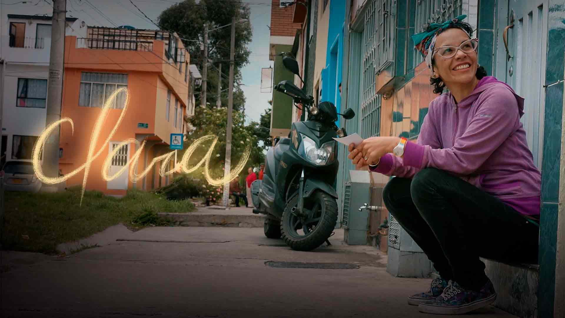 Mujer joven sonriendo sentada en el andén afuera de una casa - Clara