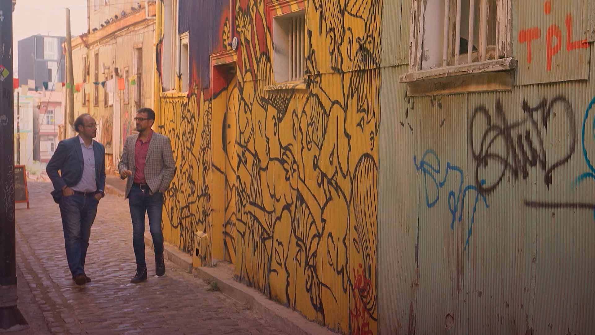 Dos hombres caminan por un callejón con las paredes están llenas de grafitis Las redes y la calle En el nombre del pueblo 