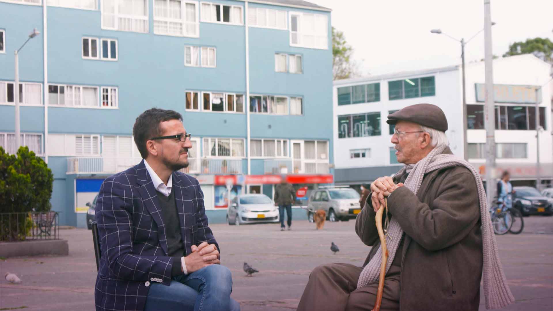 Mario Riorda conversa con un adulto mayor en el centro de una plaza En el nombre del pueblo serie documental