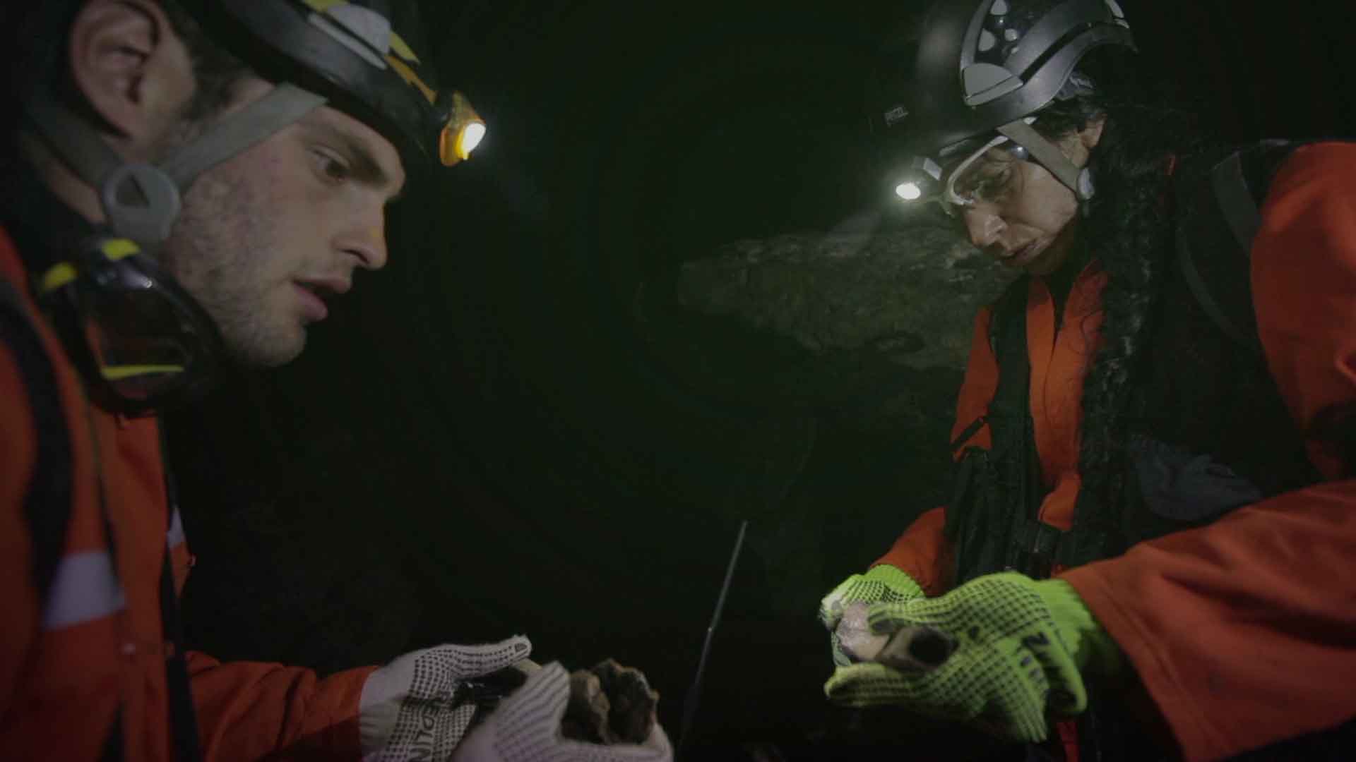 Un hombre y una mujer revisan rocas dentro de una caverna - Misión ciencia