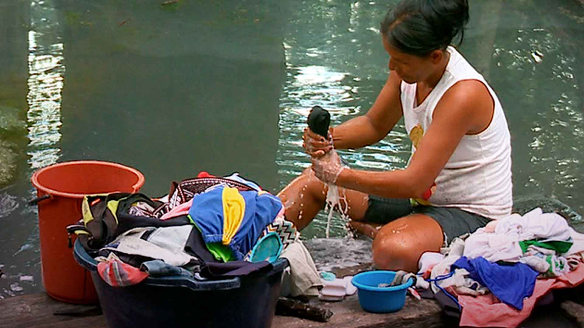 mujer lavando ropa en el río