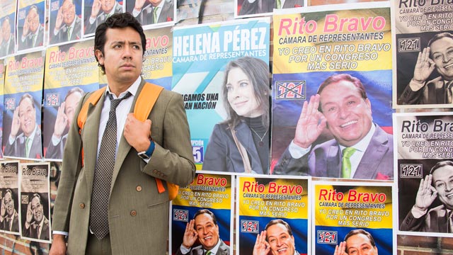 Jimmy al frente de un muro con carteles políticos, estratega digital, campañas publicitarias, campañas politicas, series de rtvcplay, series gratis, series originales de rtvcplay, series de rtvc, series online