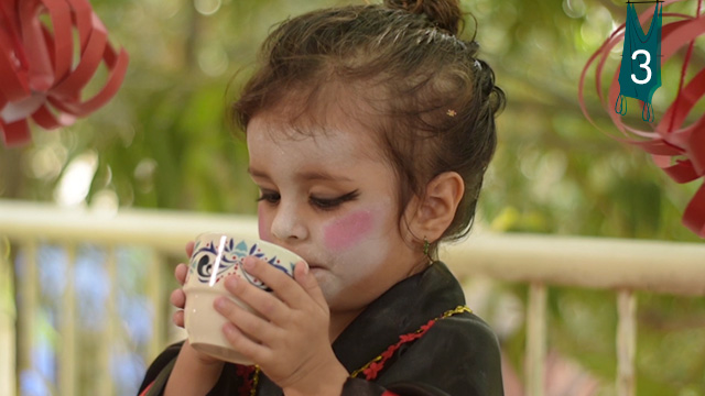 Niña disfrazada tomando refresco en un balcón