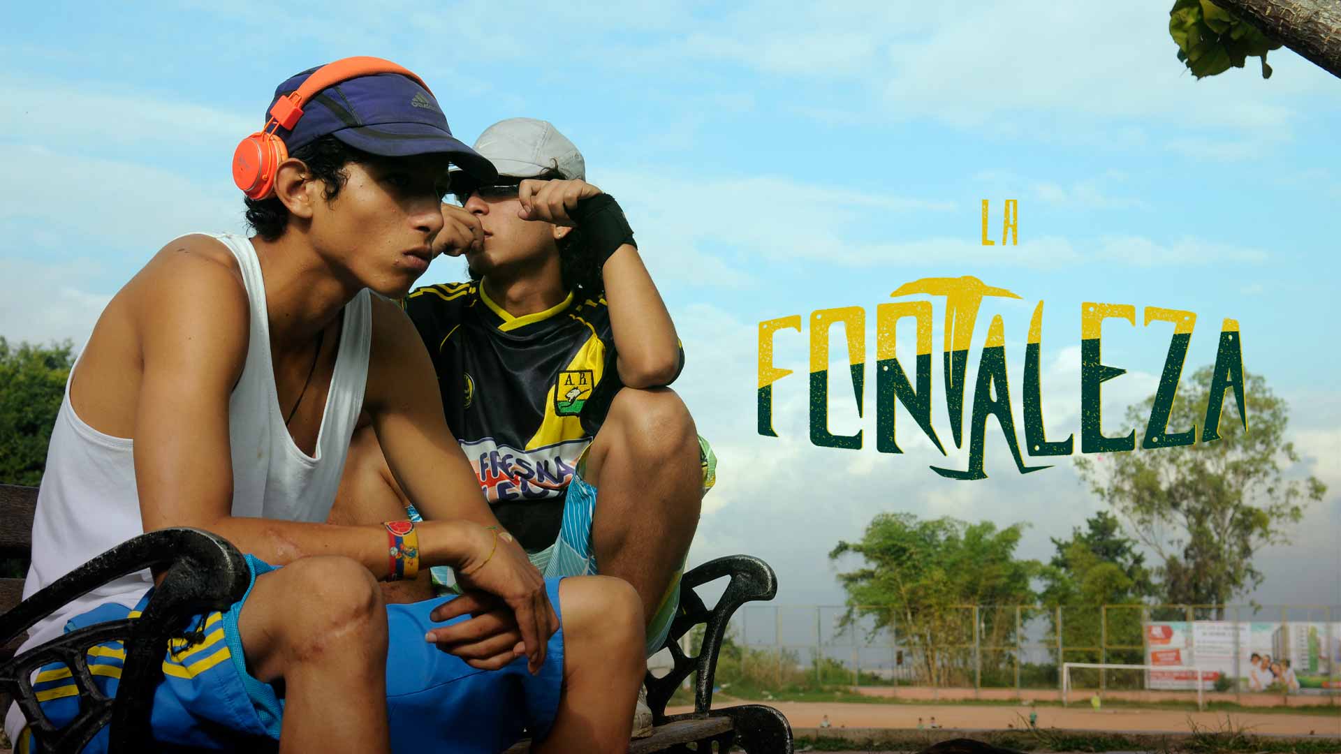 Dos hinchas jóvenes de fútbol sentados en una banca junto a una cancha de fútbol - La fortaleza