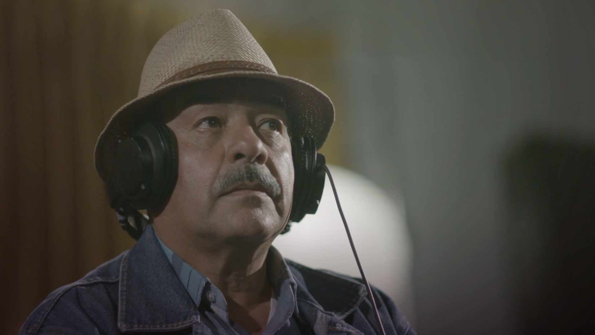 Hombre mayor con unos audífonos y sombrero dentro de estudio de grabación