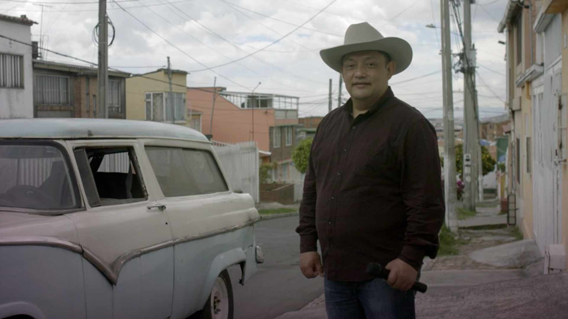 Cantante con un microfono en su mano y sombrero en una calle de la ciudad con un carro antiguo a su lado