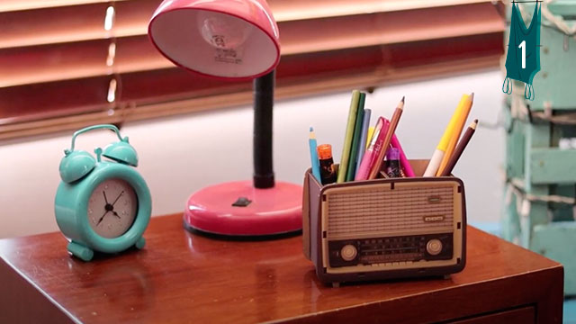 Reloj despertador, una lampara y lapiceros en una mesa de noche