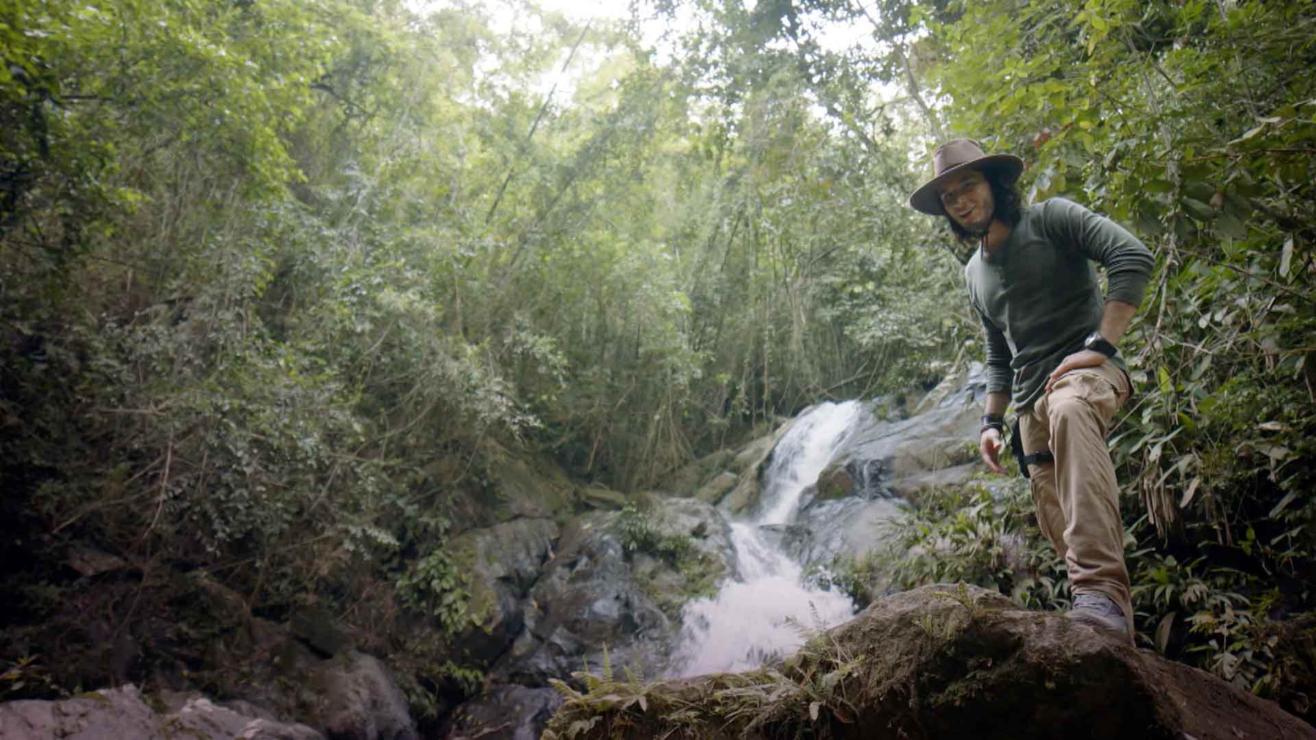 Joven al lado de la quebrada de un río en medio del bosque
