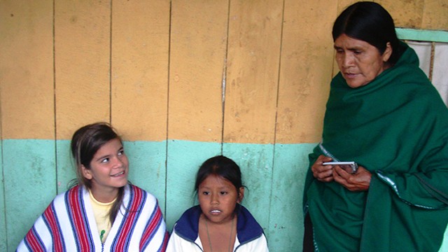 dos niñas sentadas junto a una mujer adulta mayor indígena