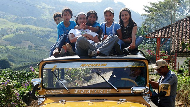 grupo de niñas subidas en el techo de un carro y atrás de ellas unas montañas