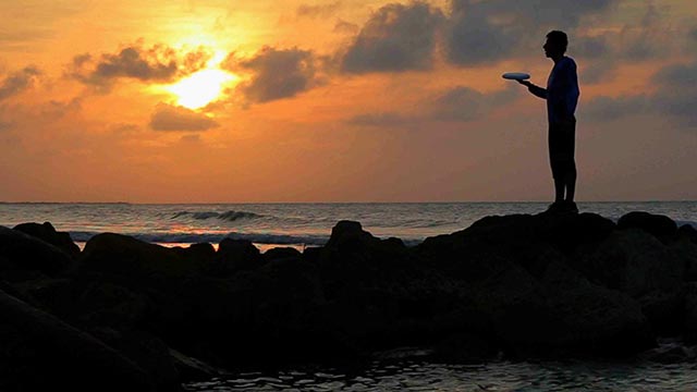 Hombre con un frisbee en una playa al atardecer - Alma del sur 
