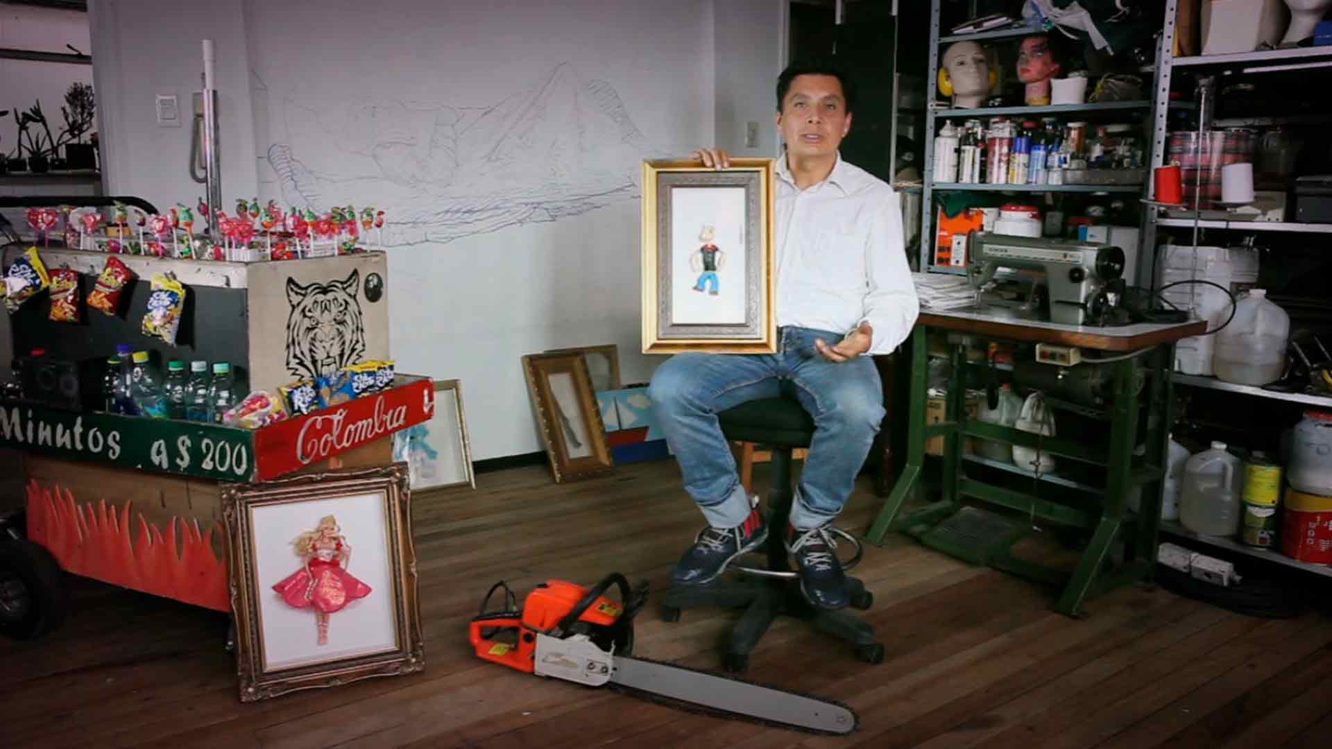 El artista William Martínez sentado en su taller sosteniendo una obra hecha a alias “Popeye” serie documental Artecámara presenta