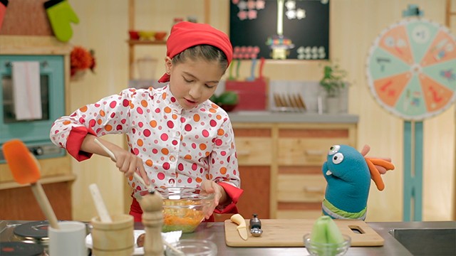 una niña chef cocinando junto a un guante de peluche