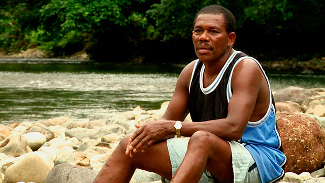 hombre moreno sentado en una roca cerca al río