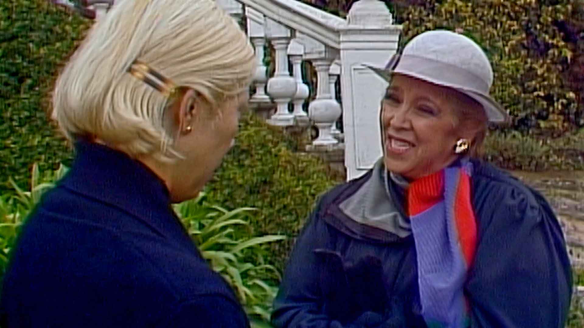 Dolores habla con una mujer en el jardín de la mansión olmedo de la serie de misterio Los cuervos