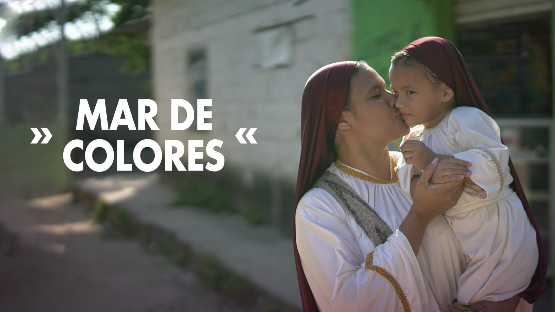 Madre perteneciente a una comunidad religiosa sosteniendo a su hija en brazos y dandole un beso en la mejilla. 